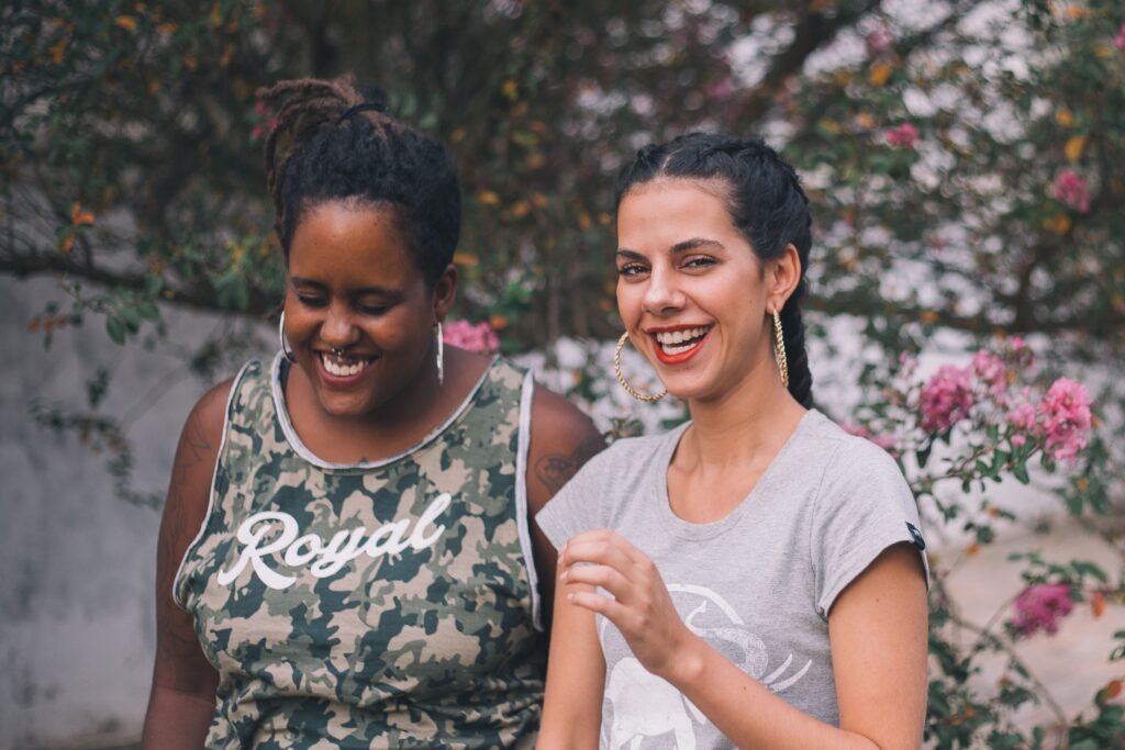 Two women smiling and laughing outdoors surrounded by nature, conveying happiness and friendship.