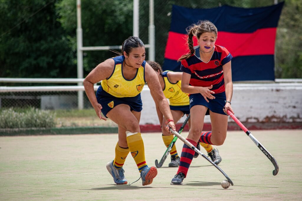 Two women playing field hockey outdoors, showcasing intense competition and teamwork.