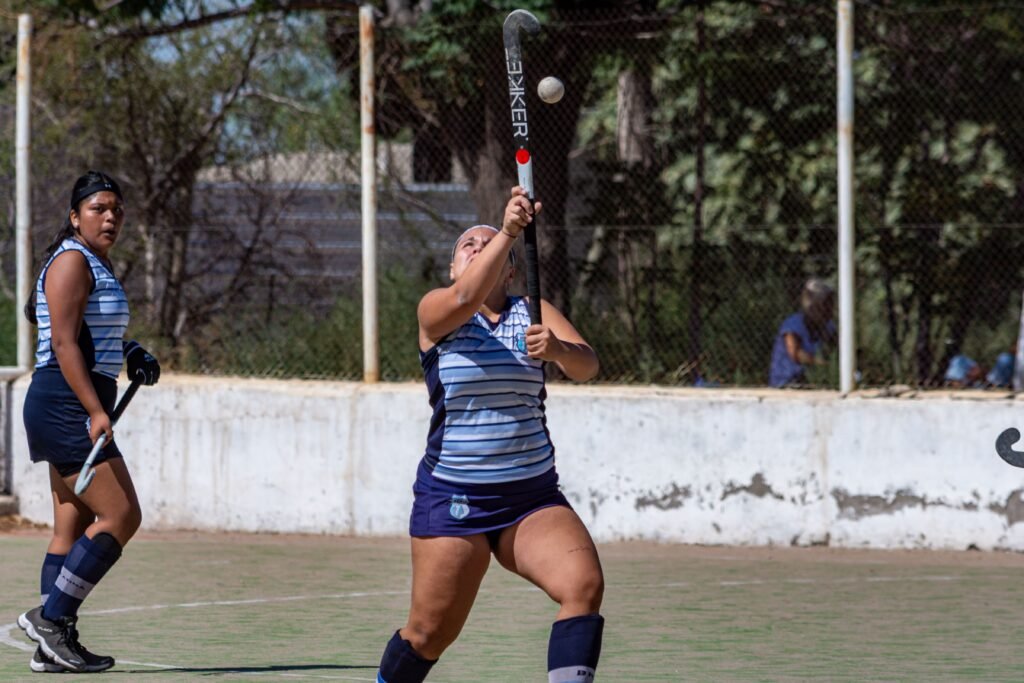 Two women playing field hockey outdoors in action with equipment.