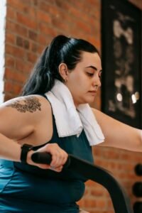 Sporto nauda TAU Side view of active plus size ethnic female with towel training on cross trainer machine during workout in modern gym